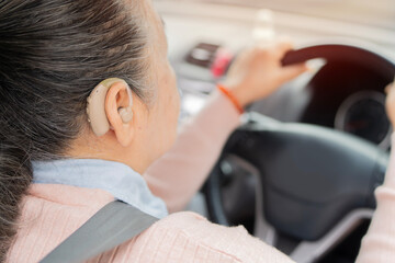 Elderly woman with hearing aid behind the steering wheel. Safe driving for elderly.