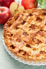 Freshly baked apple pie with red apples and leaves on green tablecloth