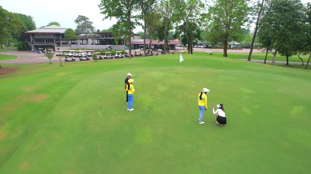 Drone view of young golfers swing clubs together on a scenic golf course. 