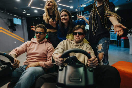 Friends gather in an arcade, engaging in a lively gaming challenge with racing simulators while sharing lots of laughs and positive energy.