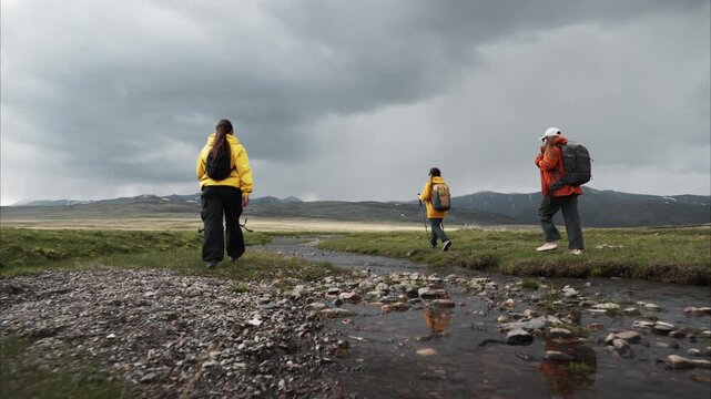 A group of female tourists walk on a high mountain plateau along a stream on a cloudy rainy autumn day. People trekking for exploring, tourism or adventure on outdoor holiday