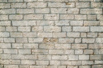 Textured wall of rectangular stone blocks in light beige shades and cement between them.
