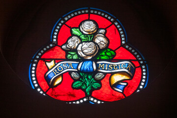 Stained glass with white mystical roses and "Rosa Mystica" ribbon on vibrant red