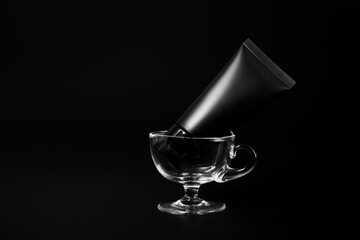 Black plastic cream tube in glass for mockup on black background. Selective Focus.