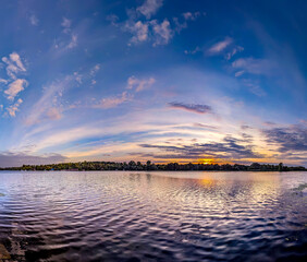 A panoramic dome of cirrus clouds. An arch of magical purple sunset with yellow and orange reflections from the sun is reflected calm waves river. A calming evening spectacle. Pink flakes of steam.