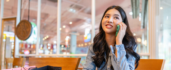 Young asian woman sitting at cafe holding coffee cup and shopping bags talking on smartphone, relaxed lifestyle, casual fashion, online communication, urban technology and modern social connection