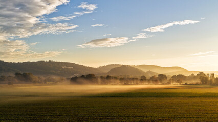 Golden Morning Mist Over Wide Farmland and Distant Hills