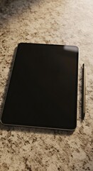 A tablet and stylus are placed on a textured surface, ready for use.