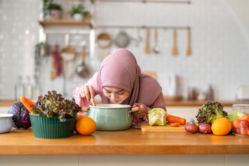 Muslim woman happy cooking healthy meal in kitchen wearing hijab making soup in pot with fresh vegetables food preparation activity nutrition, ramadan healthy recipe preparation, islamic food culture