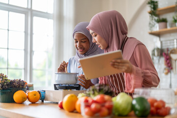 Muslim girl cooking with woman using tablet for recipe, halal food learning with technology, warm islamic family lifestyle, digital nutrition education for muslim kid, modern halal kitchen inspiration