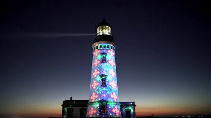 Festive Lighthouse Illuminated with Colorful Projections Under a Starry Night Sky