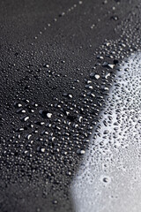Black glass surface with white spots in water droplets closeup, wet mirrored black glass in a large number of water