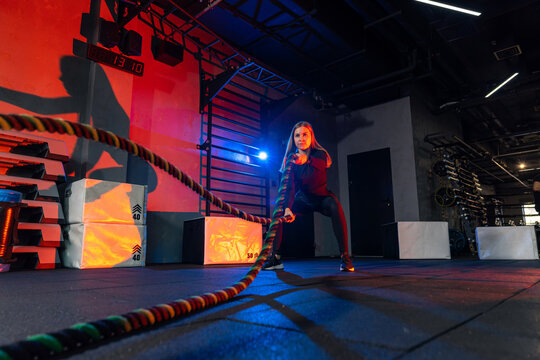 Workout session with battle ropes in modern gym setting. A woman performs an intense workout using battle ropes in a dimly lit gym. The atmosphere is energetic and focused. - Powered by Adobe