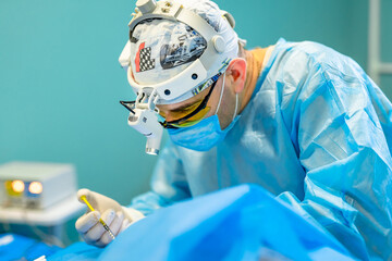 Surgeon performing a delicate procedure in a hospital. A surgeon in blue scrubs focuses on a...