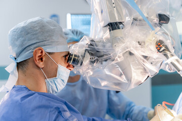 Surgeon performing delicate procedure in sterile environment. Surgeon focuses intently on a specialist machine while assisting in a surgical operation in a hospital setting.