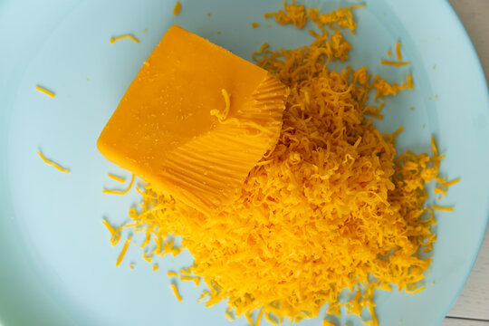 a piece of cheese and a large amount of finely grated yellow cheese made from fresh milk, grating fresh orange cheese for pizza or pasta