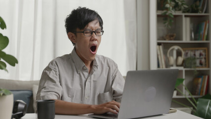 Asian man yawning while working from home.