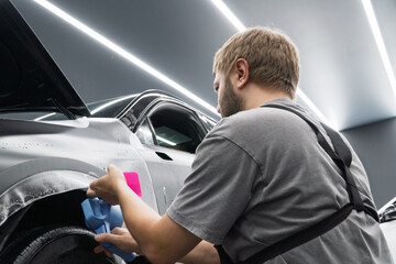 A car wrapping specialist applies a polyurethane film to the car. Car wrapping, detailing, tuning and styling. Detailer smoothes PPF. PPF protective film against chips and scratches. Selective focus.