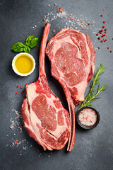 Two raw Tomahawk steaks, on the bone with rosemary, butter and salt. On a gray concrete background.