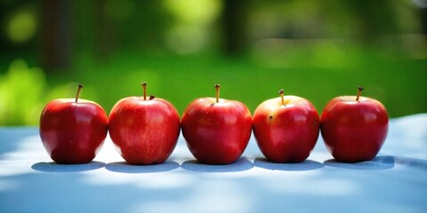 Three green apples with stems on a white surface , green trees in the background
