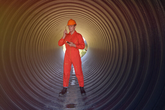 A male engineer in an orange suit is inspecting the integrity and safety of a pipeline.