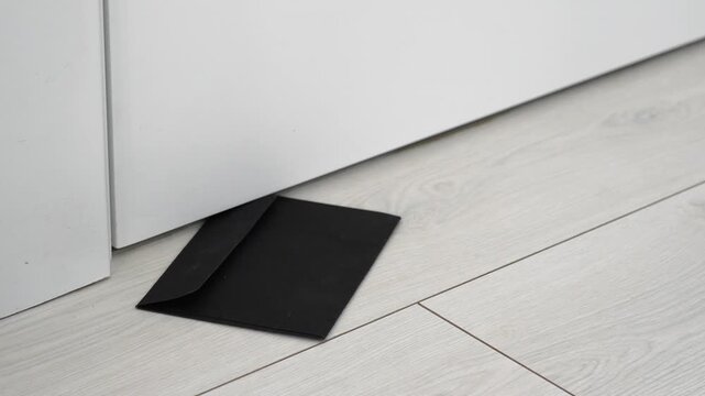 A black envelope with a message under the door.
Receiving a letter at the door.
A black envelope with a paper letter on the floor.
Letter, floor, message, mail, delivery
