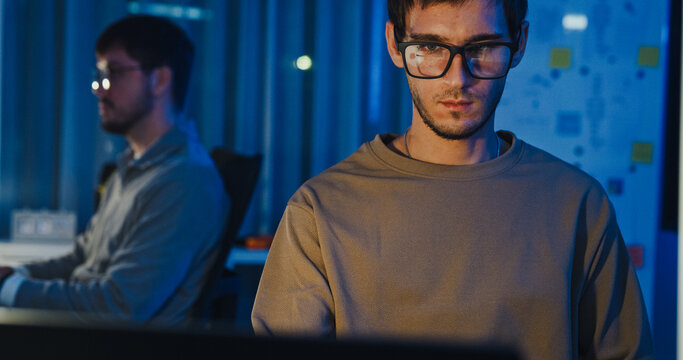 Team adult male freelance developer work late typing write prompt AI bot app program nomad terminal code at office night. Artificial intelligence dashboard, robotics, user interface, machine learning.