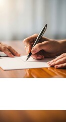 Close-up of two hands signing a document on a wooden table.