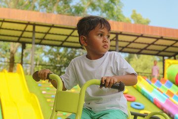 Asian boy on a yellow playground ride looks off to the side with a serious, pensive expression.