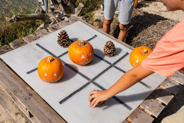 Children playing tic-tac-toe game with halloween pumpkins and pinecones