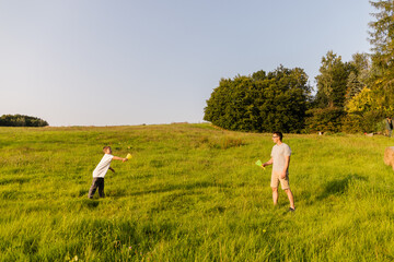 A father and son share quality time outdoors, playing catch on a sunny day. The lush green grass surrounds them as they laugh and enjoy their time in nature