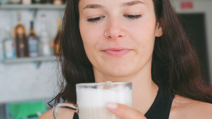 A Young Woman Enjoys a Refreshing Latte Macchiato at a Sunny Bar During a Warm Summer Morning