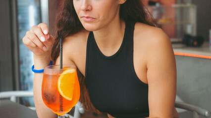 Young Woman Enjoying Refreshing Aperol Spritz Cocktail with Orange Slice and Snacks at a Cozy Bar Table on a Sunny Afternoon