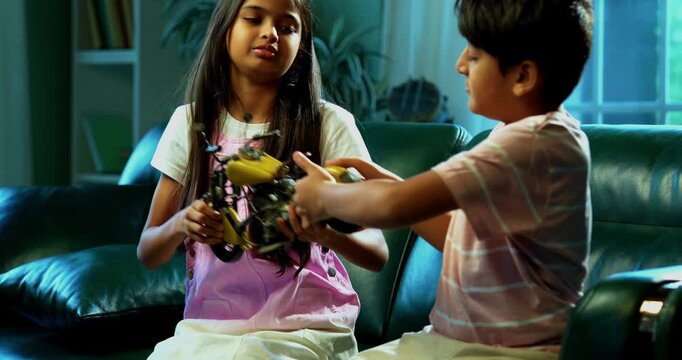 Indian Asian small sibling kids fighting over toy bike while sitting on sofa in modern home interior, one child upset while brother and sister argue, family bonding, sibling rivalry