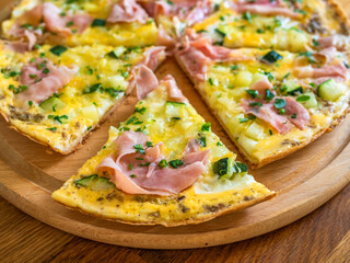 Frittata - scrambled eggs with zucchini and boiled ham on wooden table