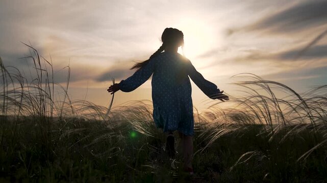 Girl walking through tall grass in field at sunset child silhouette walks with braid and dress backlit by golden sky hands brush grass horizon glow creating peaceful nature scene under warm light