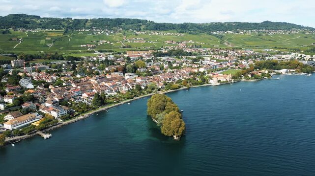 Aerial view of Rolle and the &Icirc;le de la Harpe, with the vivid contrast of the town's terracotta roofs against the deep blue lake, Rolle, Vaud, Switzerland.