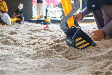 Toy cars are playing in the sand: a yellow excavator, a blue truck and an orange bulldozer. It's a...