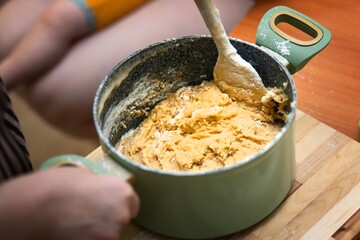 Female hand mixing thick honey dessert dough in a pot with a silicone spatula