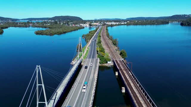 Drone aerial landscape of cars driving along main road highway bridge into Woy Woy town suburbs with train railway line running alongside Central Coast Australia travel transport infrastructure