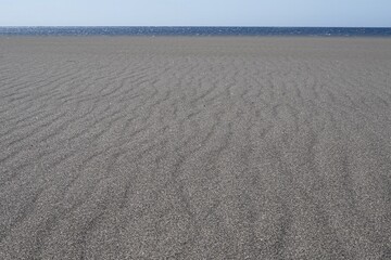 A beach with black volcanic sand, natural sand ripples and an ocean horizon