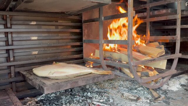 Whole turbot roasting over open flames on a traditional Argentinian-style grill, with a dramatic view of the fire and the sizzling fish