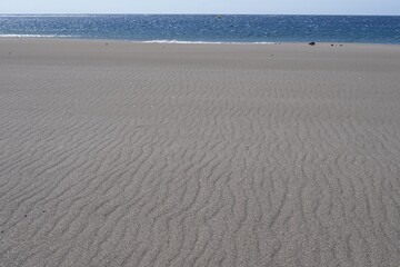 A beach with black volcanic sand, natural sand ripples and an ocean horizon