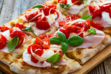 Pinsa Romana with boiled ham, cherry tomatoes, burrata cheese and basil leaves on wooden table	
