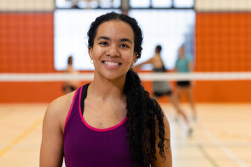 Female athlete standing and smiling at camera in sports hall with badminton ne, shuttlecock