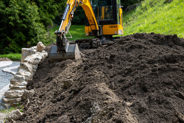Fototapeta premium Yellow excavator moving pile of soil at outdoor construction site, concept of land development, engineering projects, infrastructure and heavy industry machinery