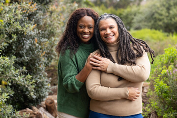 Diverse mother and daughter hugging, wearing knit turtleneck sweaters in lush garden