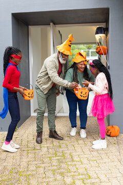 Diverse family handing out Halloween candy into pumpkin buckets at front porch with decorations