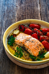 Oven baked salmon steak with cherry tomatoes in baking dish on wooden background