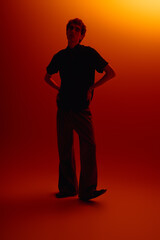 Stylish young man showcases modern fashion in a vibrant orange glow